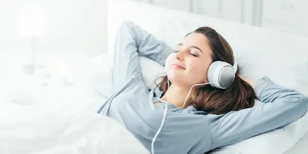 خانمی در تخت خواب در حال گوش دادن به موزیک و لذت بردن است.